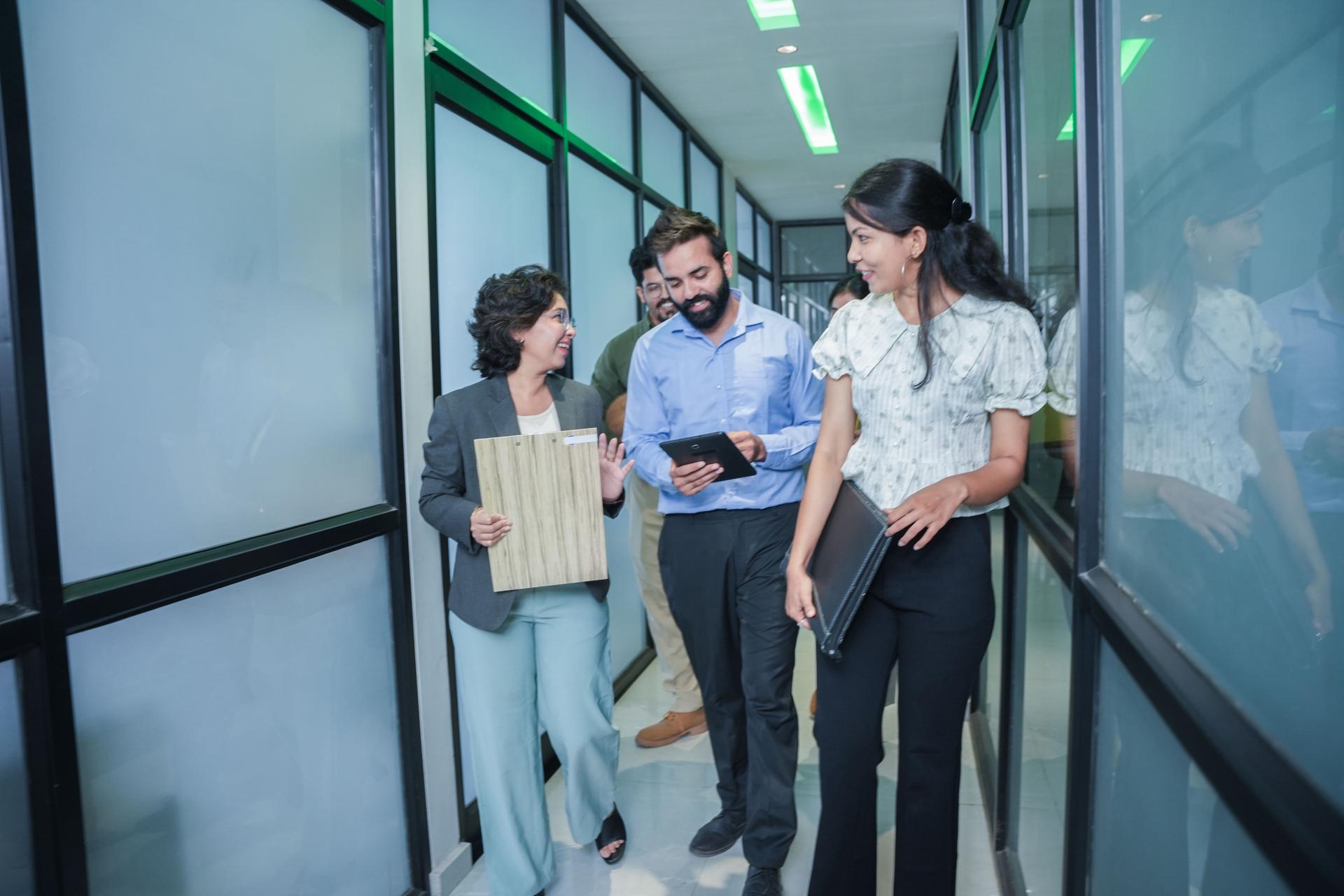 group of young indian corporate business people in formal wear holding reports or documents in hand having a discussion before the meeting while walking through the office. Teamwork and workspace