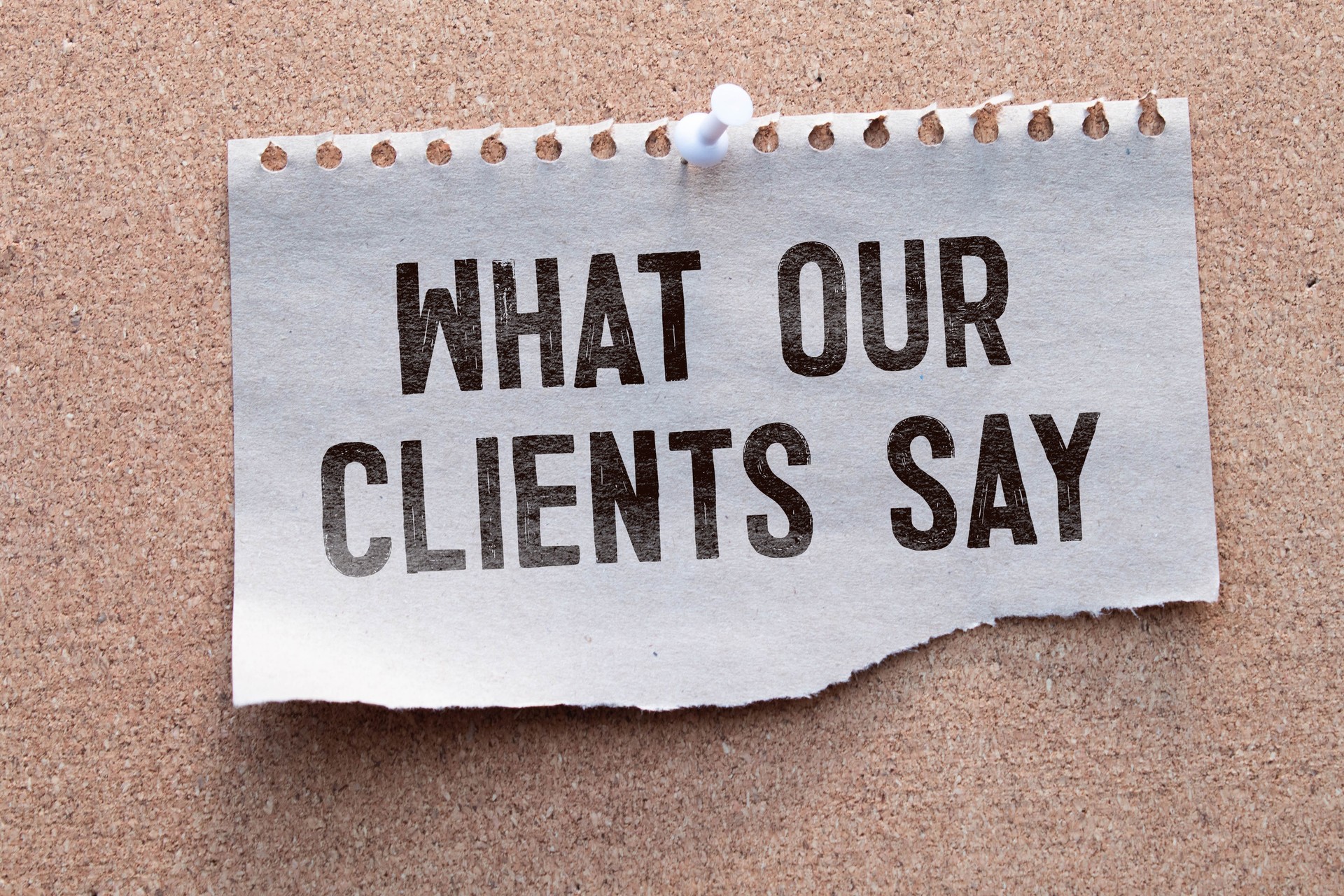 What Our Clients Say statement on paper note pad. Office desk with electronic devices and computer, wood table from above, concept image for blog title or header image.